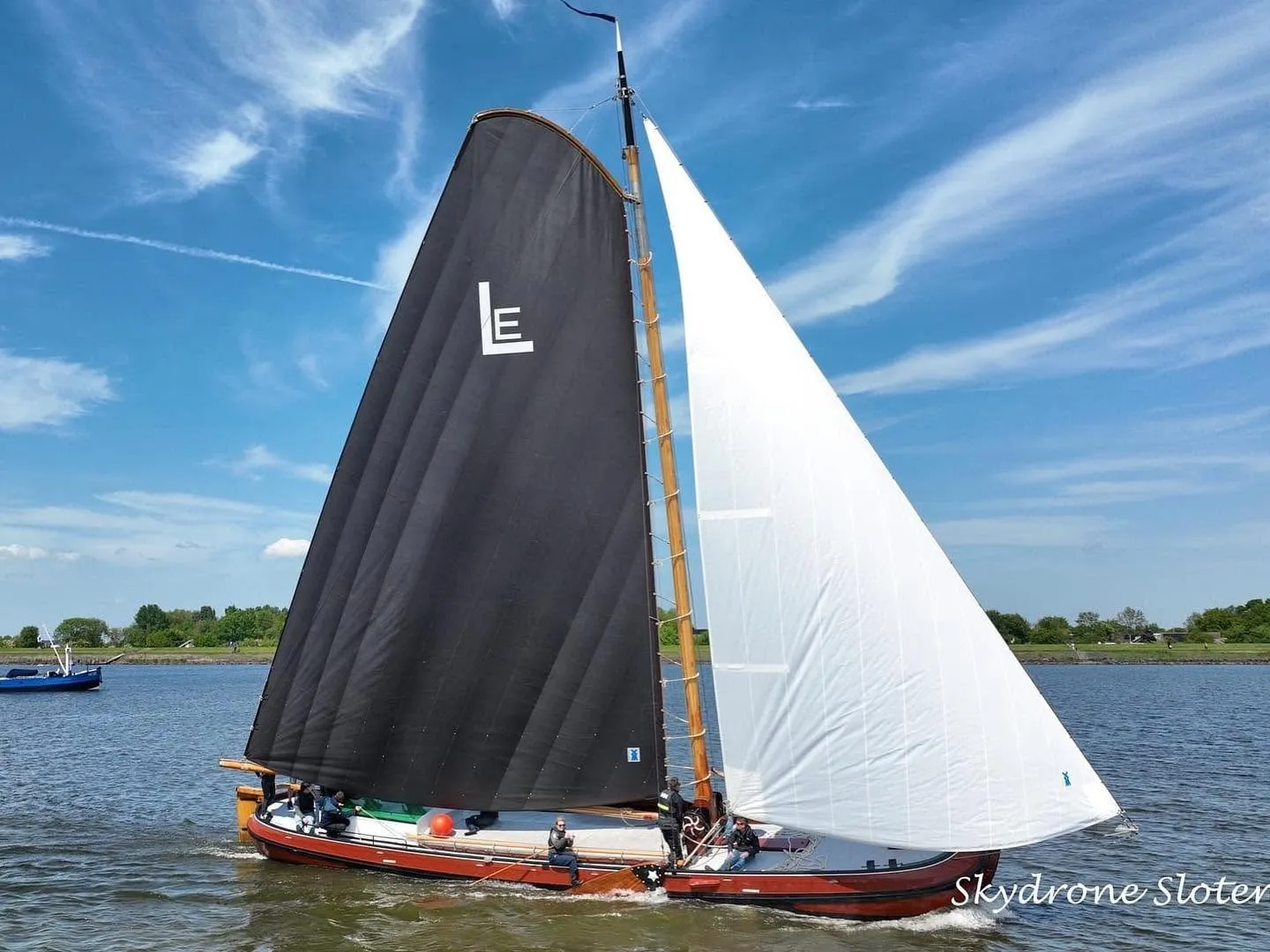 Lytse Earnewâldster van opzij, met de bemanning langs de rode romp en het LE-teken in het zeil.